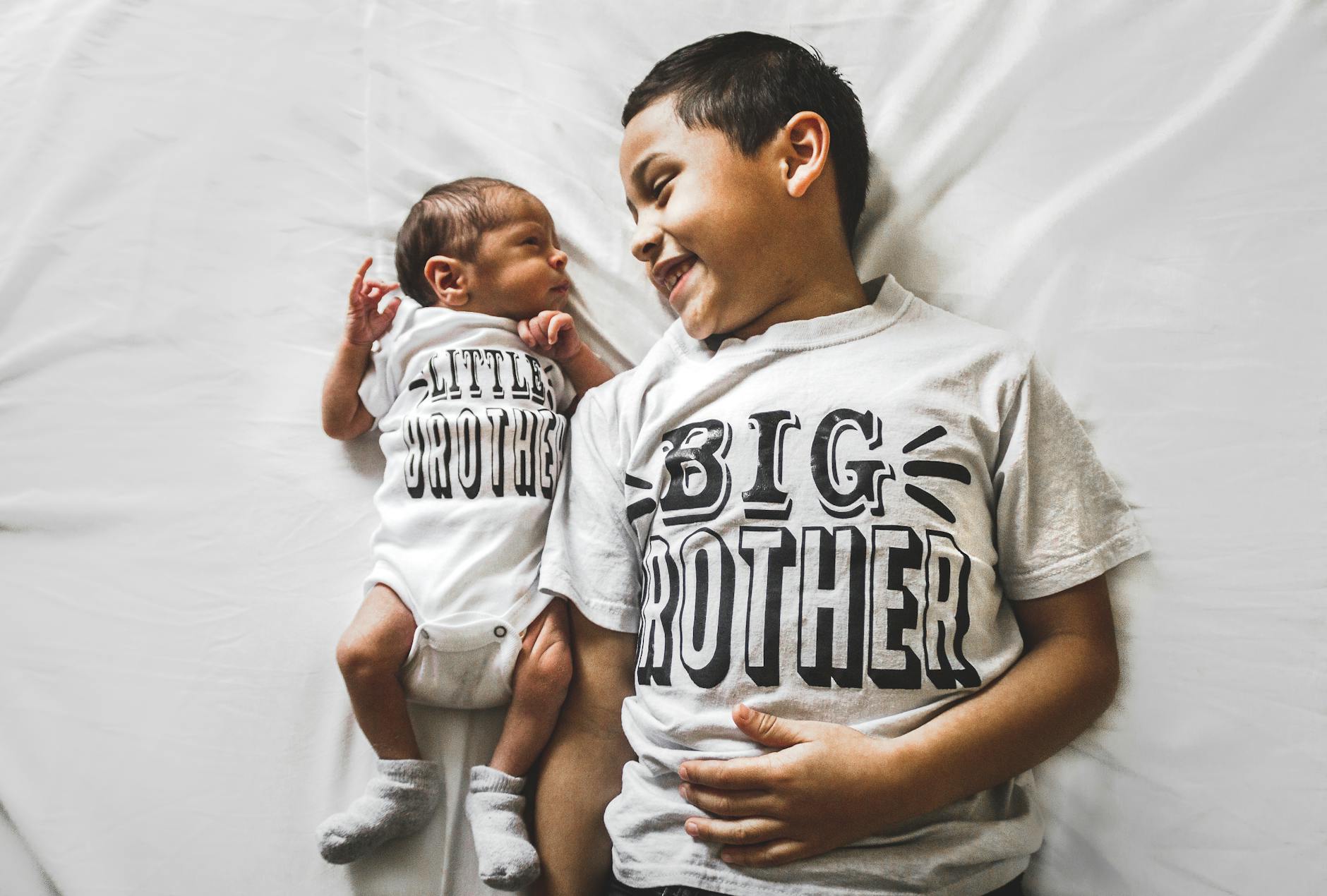 Starszy brat trzyma noworodka, oboje w pasujących koszulkach