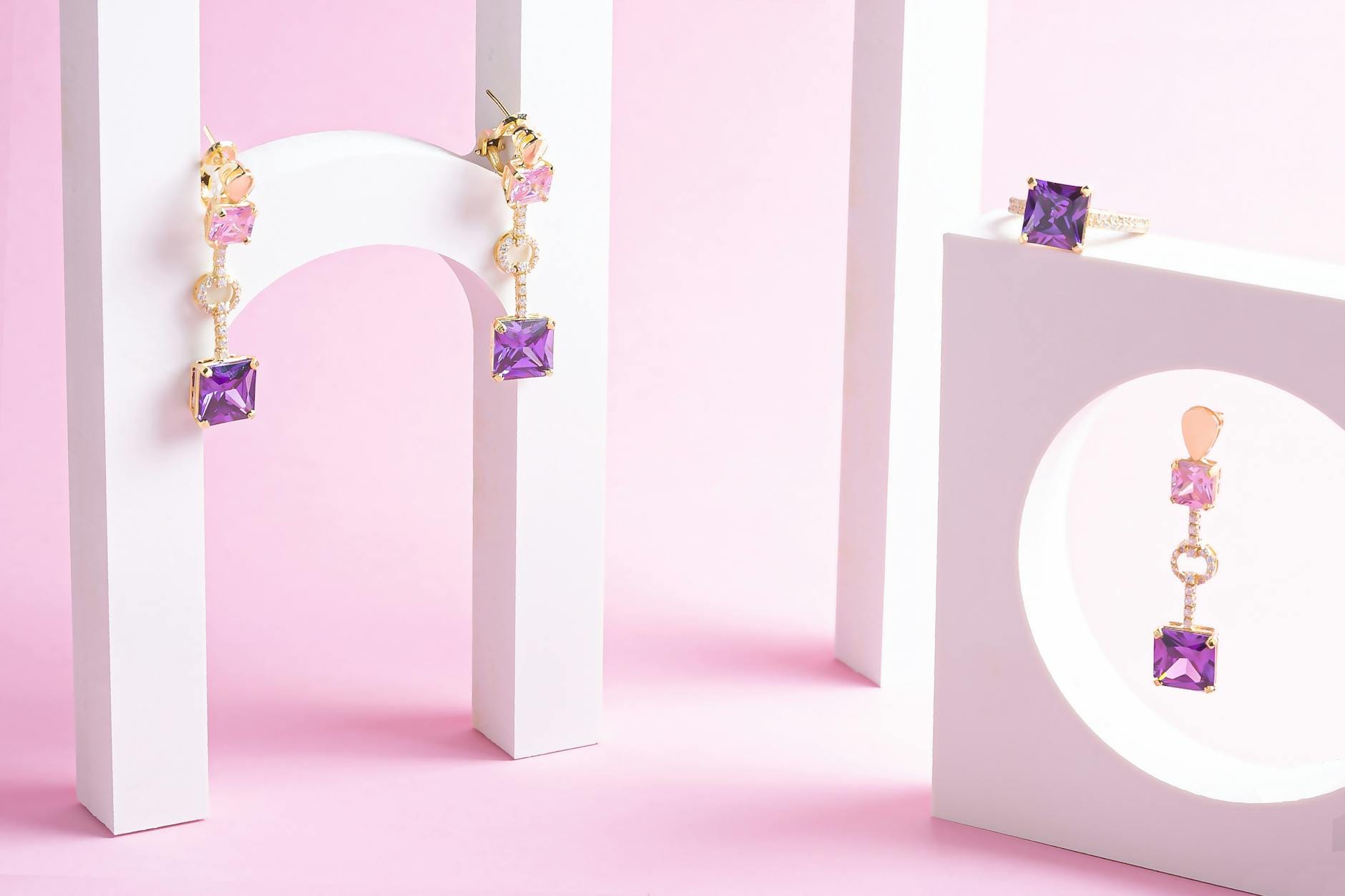 Złota minimalistyczna biżuteria z fioletowymi kamieniami na różowym tle