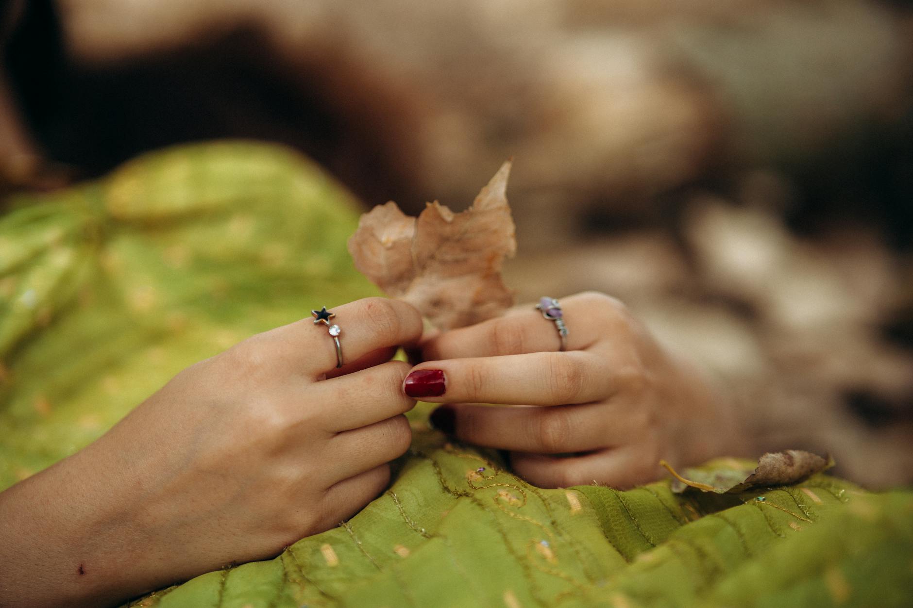Dłonie z ozdobnymi pierścionkami trzymające jesienny liść