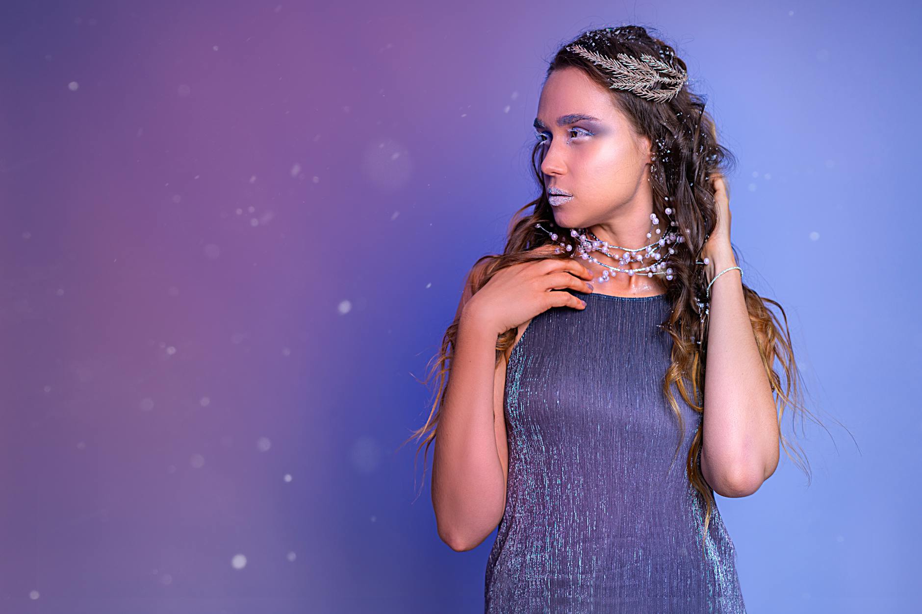 Kobieta w metalicznej sukience z perłową biżuterią na fioletowym tle